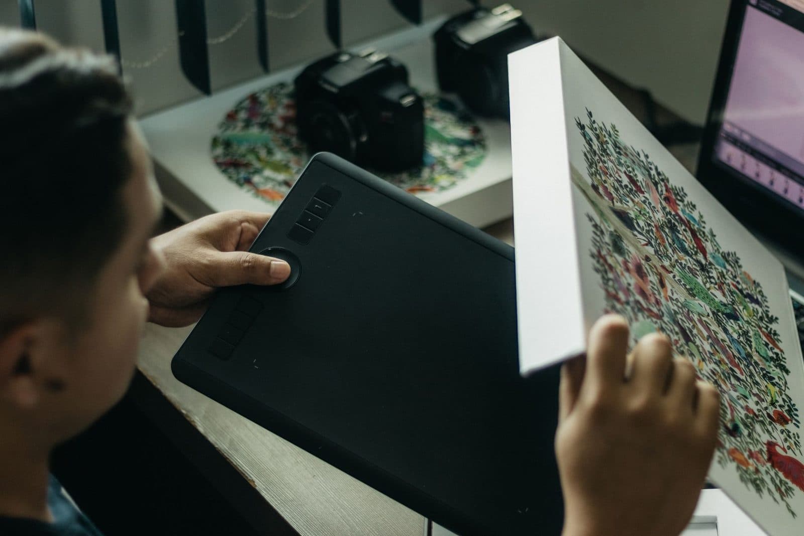 Graphic designer at work reviewing a printed illustration with a drawing tablet